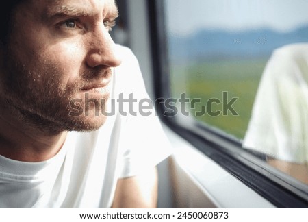 Close up picture of a young serious man looking out of the window in a train