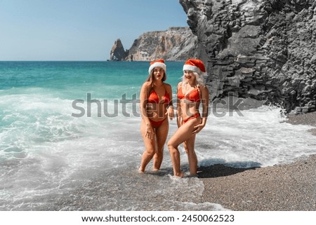 Women in Santa Claus hats run into the sea dressed in red swimsuits. Celebrating the New Year in a hot country