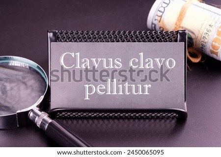 Clavus clavo pellitur. The ancient Greek expression translates as, A wedge is knocked out with a wedge. on the business card next to a roll of money and a magnifying glass on a black background