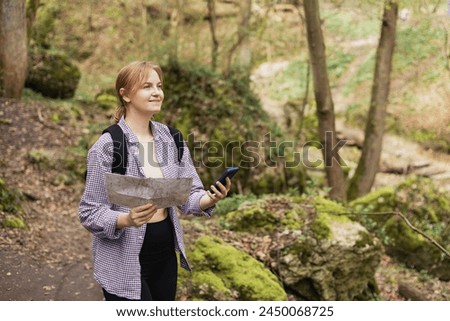 Solo tourist Woman with paper map and smartphone hiking on footpath in spring forest. Person in sport clothes walking on nature background. Wanderlust travel concept, atmospheric moment, earth day