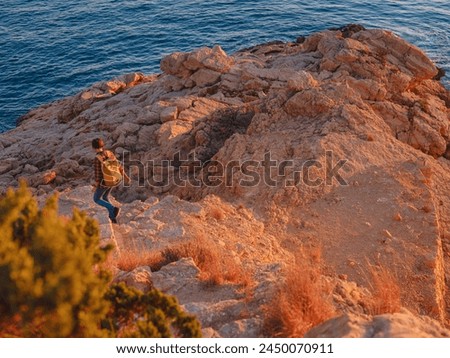 Young woman hiking on rocky beach in Spain, Benidorm. Watching the choppy sea and the bay. traveler enjoying freedom in serene nature landscape Royalty-Free Stock Photo #2450070911