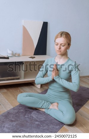 A young woman in a tracksuit on a mat while meditating at home.