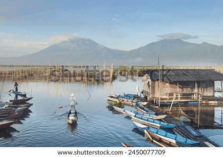 A fisherman is rowing a boat among a row of colorful boats in Wellsup Rawapening, Semarang, Central Java, Indonesia. mountain background Royalty-Free Stock Photo #2450077709