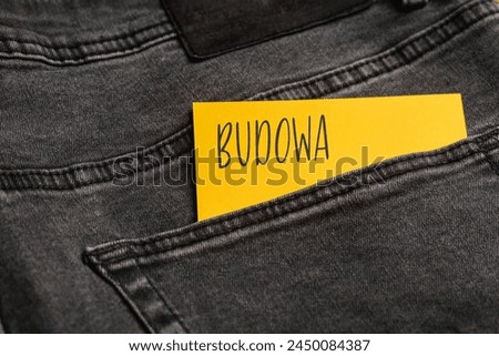 Yellow card with a handwritten inscription "Budowa", inserted into the pocket of gray pants jeasnow (selective focus), translation: build