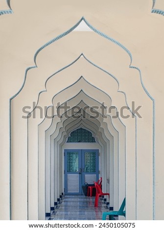 Interior diminishing perspective view of hallway along with gable partitions wall and plastic chairs inside Bang O mosque leading into entrance blue door.Mosque architecture and art concept,Copy space Royalty-Free Stock Photo #2450105075