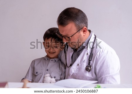A young boy is sitting on a chair with a doctor. The boy is holding a stuffed animal