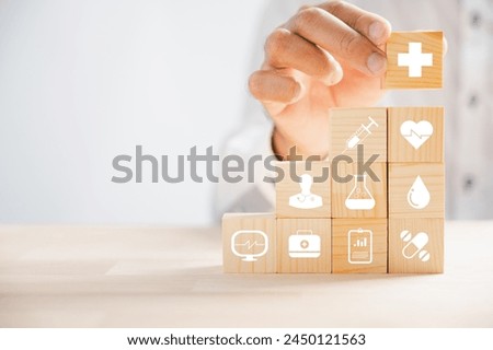 Hand clutches wooden block adorned with healthcare and medical icons, symbolizing safety, health, and family well-being. Evoking pharmacy, heart care, and happiness. health care concept