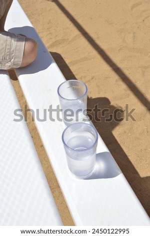 It is important to stay hydrated during a hot weather. Picture depicts two reusable plastic cups of water on a white bench. 
