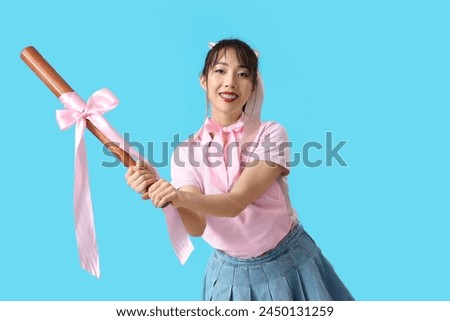 Young Asian woman with pink bows and bat on blue background