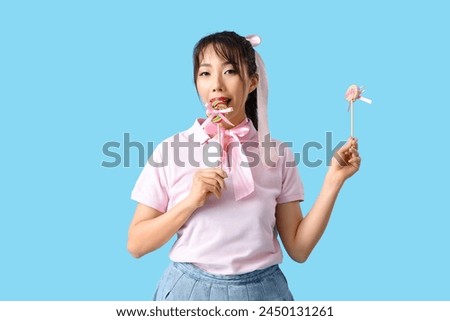 Young Asian woman with pink bows and lollipops on blue background