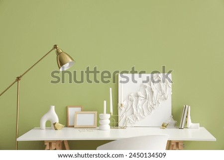 Stylish workplace with candles, blank picture frames and decor near color wall