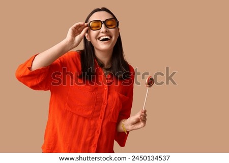 Happy young woman in sunglasses with sweet lollipop on brown background