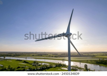 Sun behind wind turbine in The Netherlands part of Dutch 
sustainable industry along river IJssel and Twentekanaal waterway picturesque landscape. Aerial circular economy concept Royalty-Free Stock Photo #2450134839