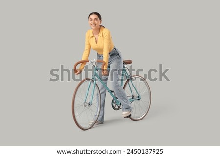 Beautiful young woman riding bicycle on grey background
