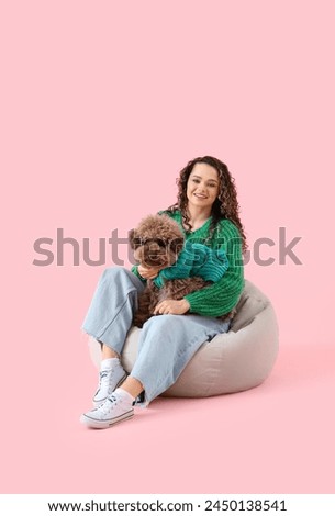 Young woman with cute poodle sitting on pink background