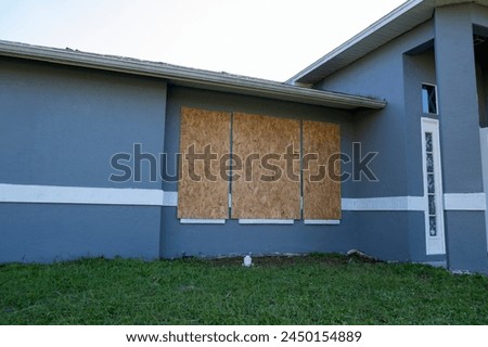 Plywood mounted as storm shutters for hurricane protection of house windows. Protective measures before natural disaster in Florida Royalty-Free Stock Photo #2450154889