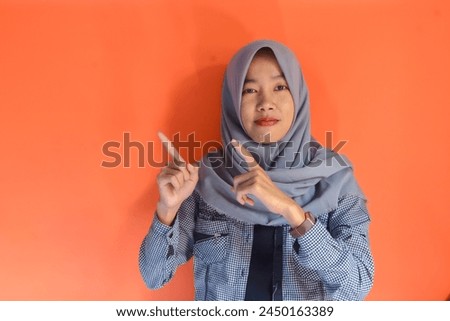 Beautiful young Asian business woman wearing black shirt and gray hijab smiling, showing, with pointing hand gesture isolated on orange background