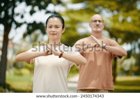Smiling man and woman doing fist palm salute when practicing tai chi Royalty-Free Stock Photo #2450174343