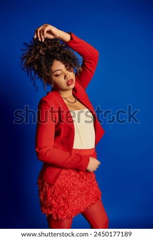 debonair african american woman in vibrant attire with collected hair looking away on blue backdrop Royalty-Free Stock Photo #2450177189