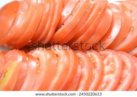A plate of sliced red tomatoes. The slices are arranged in a neat stack, with some overlapping each other. The plate is placed on a table, and the image conveys a sense of freshness and abundance