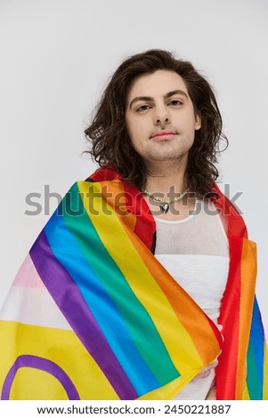 good looking joyous gay man with long dark hair posing with rainbow flag and looking at camera