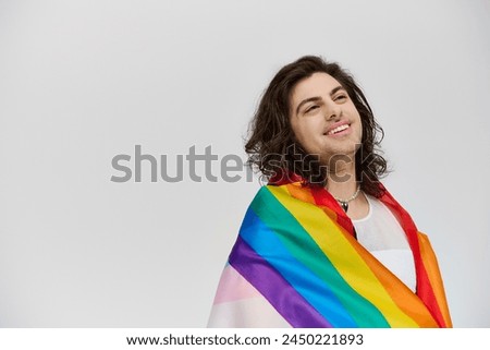 good looking fancy jolly gay man in vivid attire with rainbow flag looking away on gray backdrop