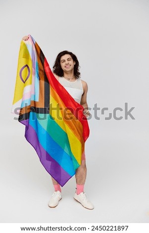 handsome joyous gay man with long dark hair posing with rainbow flag and looking at camera