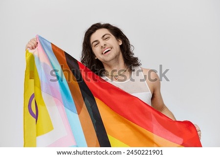 attractive joyous gay man with long dark hair posing with rainbow flag and looking at camera