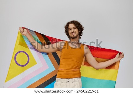 contented alluring gay man with dark hair holding rainbow flag and smiling happily at camera