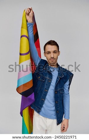 merry handsome gay man in vibrant casual attire holding rainbow flag and smiling at camera
