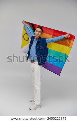 positive appealing gay man in vibrant casual attire holding rainbow flag and smiling at camera