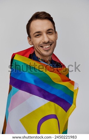 appealing cheerful gay man in vibrant casual attire holding rainbow flag and smiling at camera