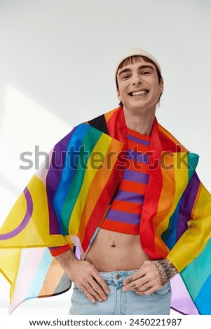 handsome jolly gay man in vivid outfit with white hat holding rainbow flag and looking at camera