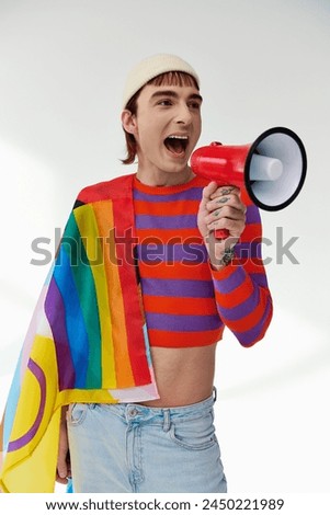 jolly stylish gay man in vibrant attire with rainbow flag using megaphone and looking away