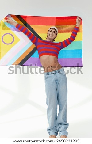 positive appealing gay man in vivid outfit with white hat holding rainbow flag and looking at camera