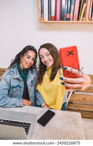 Vertical image. Two smiling American and Latina friends taking a photo with their mobile phones. Lifestyles concept.