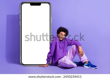 Full size photo of cheerful person wear violet hoodie sitting near smartphone screen empty space isolated on purple color background