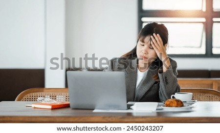 Young woman in professional attire feeling exhausted while working at her desk, with a laptop and documents.