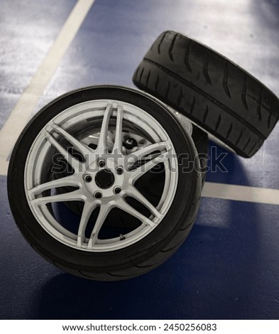 Detail of three sports car wheels stacked on the parking lot floor, white 6-spoke wheels with Semislick tires in vertical format Royalty-Free Stock Photo #2450256083