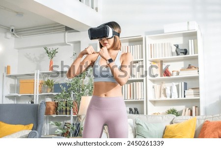 Asian healthy sportive woman wearing sportswear, VR glasses, playing game, standing in indoor living room at cozy home, doing body combat, boxing, exercising. Technology, Sport, Lifestyle Concept