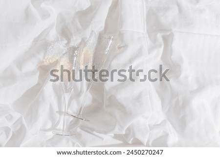 Rainbow color shining champagne glasses on bed, white blanket background. Lifestyle aesthetic photo, star filter effect. Romance meeting, romantic holiday concept. Top view minimal style light photo