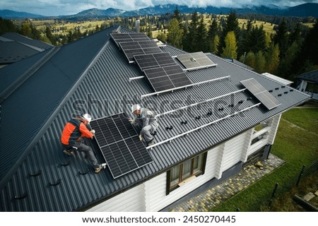 Technicians building photovoltaic solar module station on roof of house. Men roofers in helmets installing solar panel system outdoors. Concept of alternative and renewable energy. Aerial view. Royalty-Free Stock Photo #2450270445