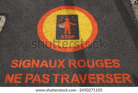 Safety warning sign painted on a sidewalk at a railroad crossing in France. French language warns pedestrians do not cross when the signal is red.