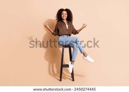 Full size photo of positive woman dressed brown shirt sit on chair palms hold products empty space isolated on beige color background