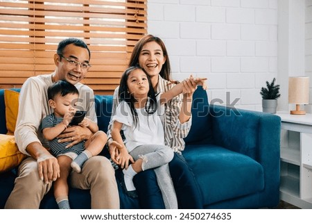 Amidst a modern setting a young family finds happiness and togetherness watching TV at home. The father mother brother and sister enjoy quality family time on the sofa.