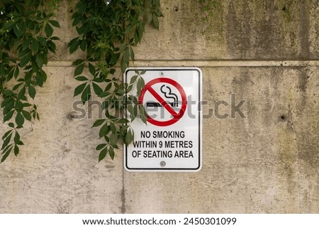No smoking sign - affixed to a concrete wall - partially obscured by overgrown green leaves