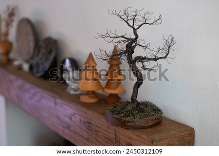 Mantle thick wood shelf above fireplace black wood-burning fire stove trees picture frame tiny candlesticks wooden vase dried flowers ceramic carvings wire tree objects living room lamp coffee table