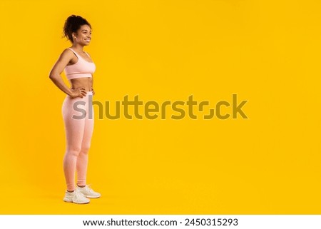 A toned african american woman poses in fitness wear with hands on her hips, isolated on a yellow background, copy space Royalty-Free Stock Photo #2450315293
