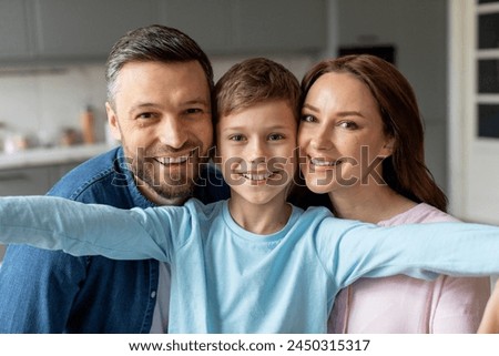 Smiling parents with child in casual clothing hugging and posing happily in a bright, contemporary kitchen setting
