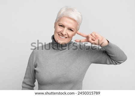 Cheerful senior european woman flashes a peace sign near her eye, portraying a playful s3niorlife moment Royalty-Free Stock Photo #2450315789